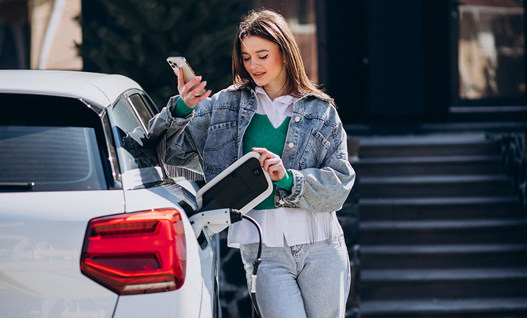 mujer cargando su vehículo eléctrico color blanco