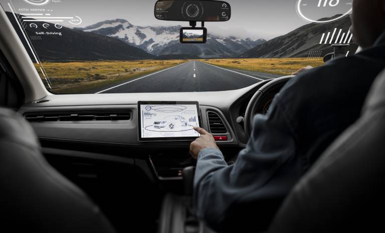 Hombre manejando la pantalla táctil de su carro mientras conduce por una gran vía con montañas de fondo.