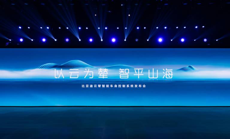 Evento de BYD, se aprecia una pantalla gigante de fondo azul y letras blancas en chino, con luces azules en la parte superior.