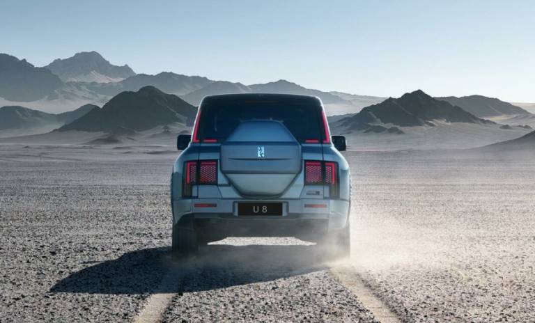 Vista trasera con la marca de rueda del YangWang U8 estacionado en un desierto.