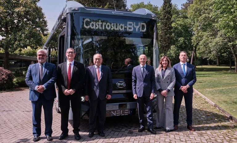 Directivos de BYD y Castrosua posando delante del bus y con árboles de fondo. 