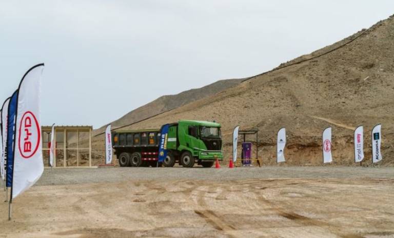 Camión de BYD verde estacionado sobre zona con arena y piedras con banderines de las compañías Enel X Way y Condestable.