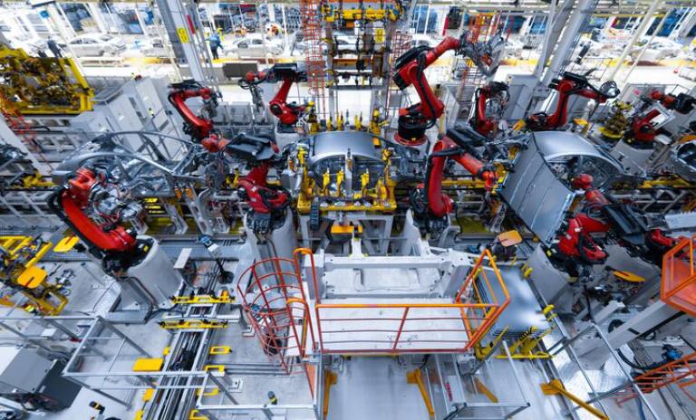 Varios robots de color rojo trabajando en la construcción de vehículos en una fábrica.